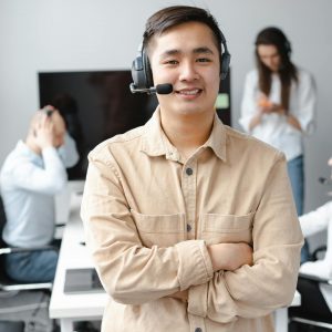 Asian call center agent smiling confidently in a modern office setting.
