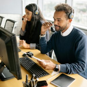 Two diverse call center agents working together at their desks with headsets in a bright office.